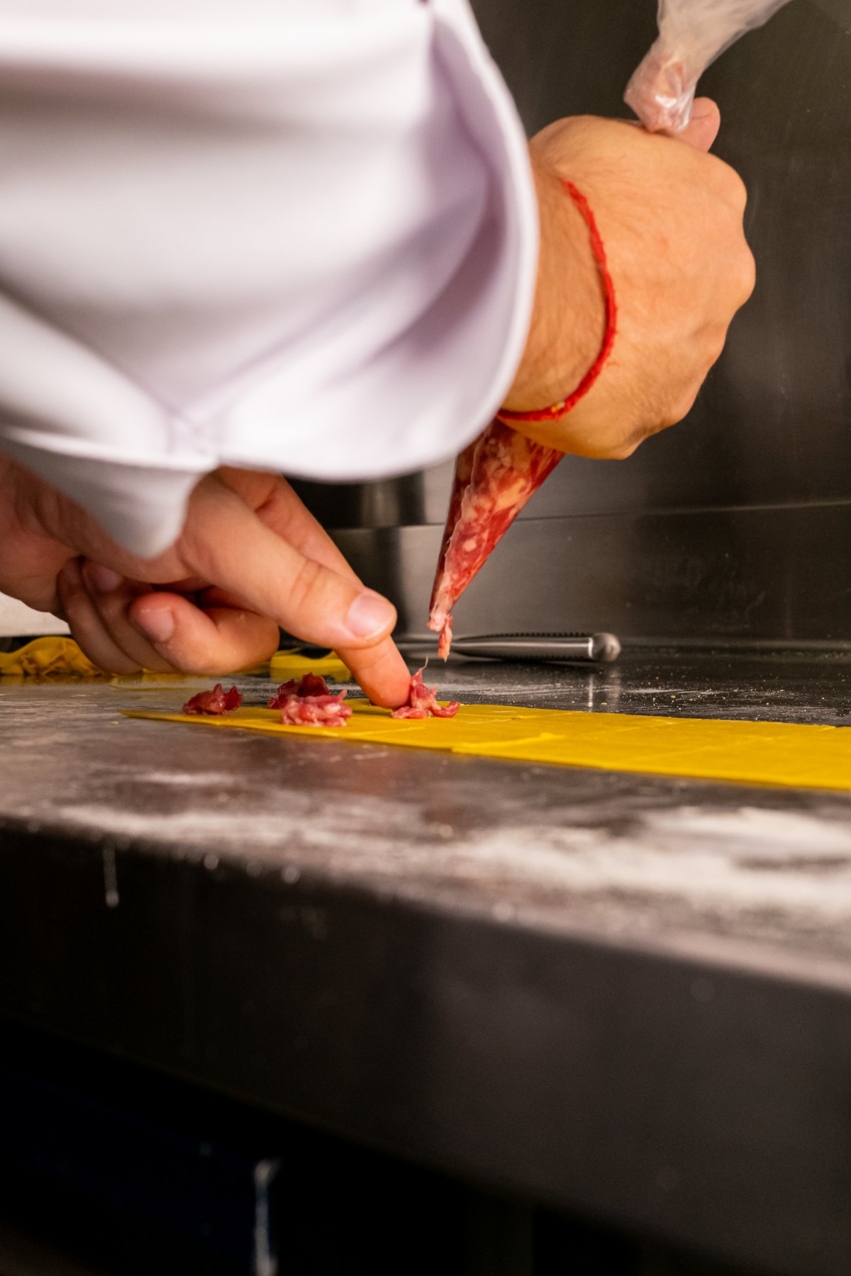 Lo chef pizzica del ripieno di salame su una sfoglia di pasta gialla in cucina